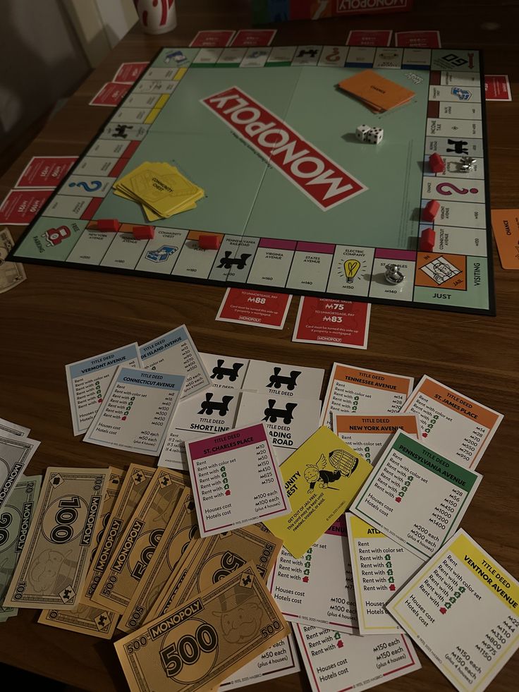 A Monopoly board game set spread out on a wooden table, with the green game board, red Monopoly logo, play money, property cards, and player tokens visible.